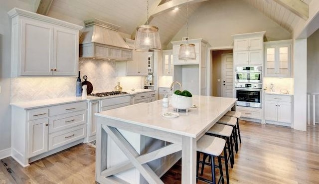 kitchen with custom exhaust hood, white cabinets, decorative backsplash, beam ceiling, and stainless steel appliances