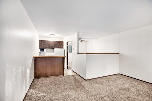 kitchen with light carpet, kitchen peninsula, ceiling fan, and refrigerator