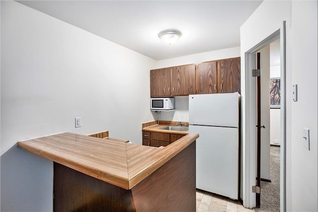 kitchen with white appliances, kitchen peninsula, and sink