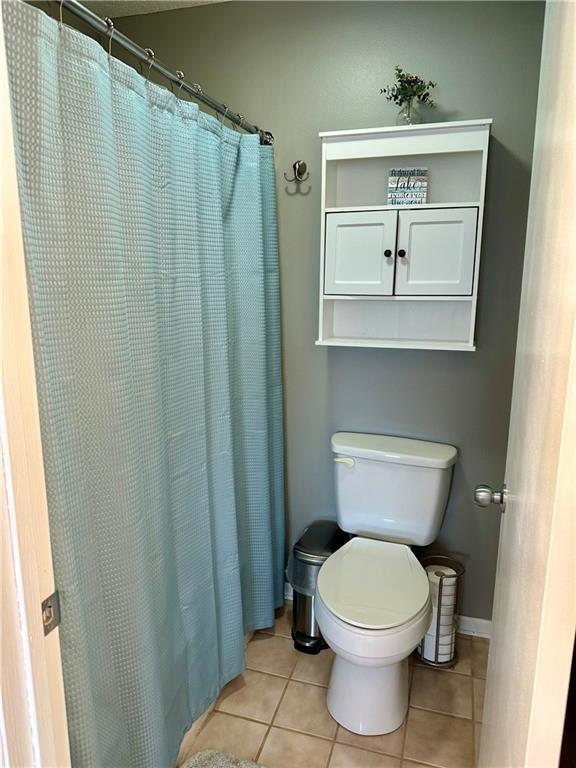 bathroom featuring tile patterned flooring, curtained shower, and toilet