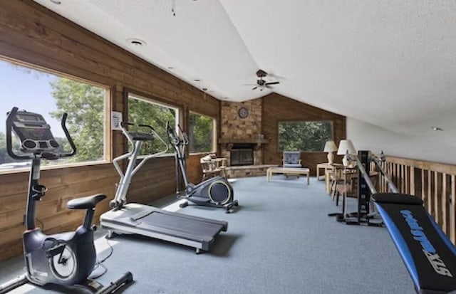 workout room featuring ceiling fan, a fireplace, lofted ceiling, and wooden walls