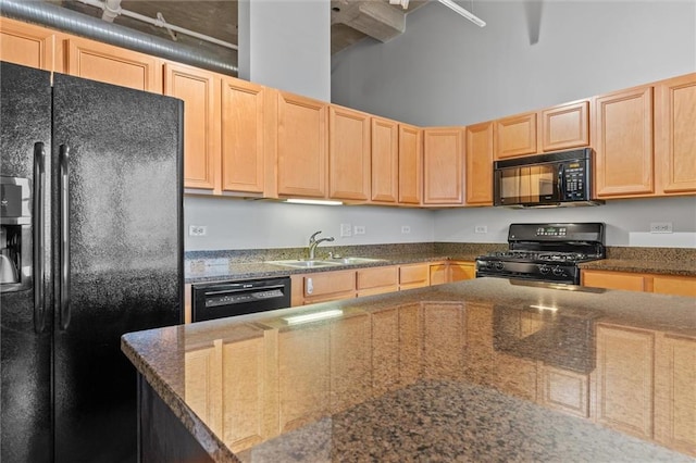 kitchen with sink, light brown cabinets, a towering ceiling, dark stone counters, and black appliances