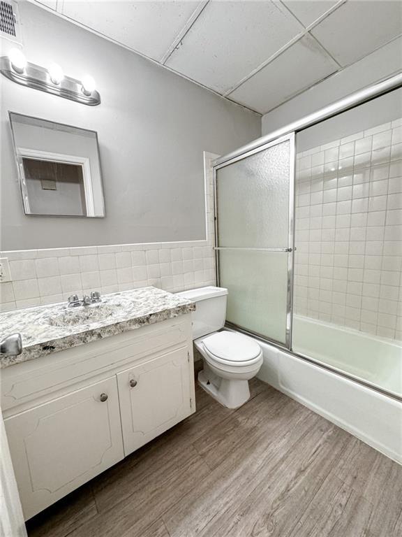 full bathroom featuring hardwood / wood-style floors, bath / shower combo with glass door, toilet, a paneled ceiling, and vanity