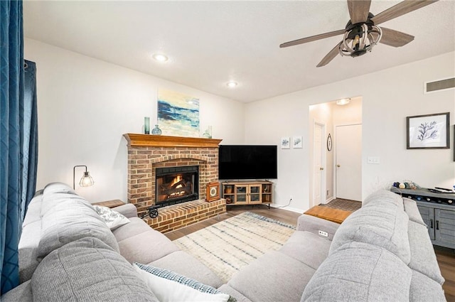 living room with a brick fireplace, dark hardwood / wood-style floors, and ceiling fan