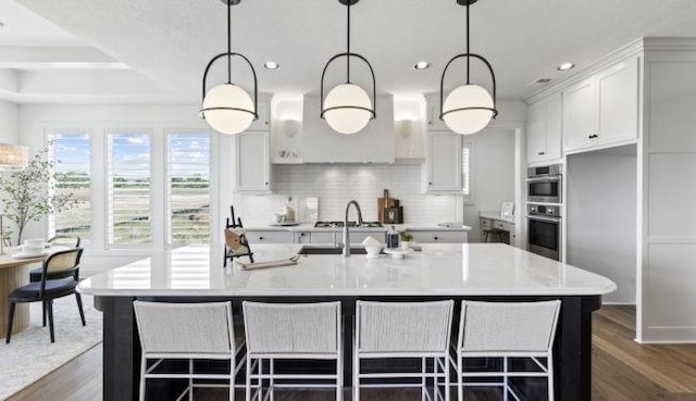 kitchen with dark wood-type flooring, a center island with sink, white cabinets, and decorative light fixtures