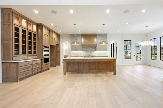 kitchen featuring custom exhaust hood, decorative light fixtures, double oven, light hardwood / wood-style floors, and decorative backsplash