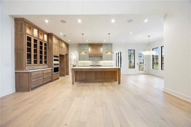 kitchen featuring decorative light fixtures, tasteful backsplash, light hardwood / wood-style flooring, custom range hood, and a spacious island