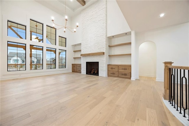 unfurnished living room featuring built in shelves, an inviting chandelier, a fireplace, light hardwood / wood-style floors, and a high ceiling