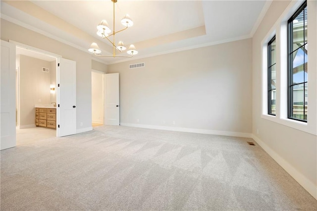 spare room featuring light colored carpet, ornamental molding, a tray ceiling, and a chandelier