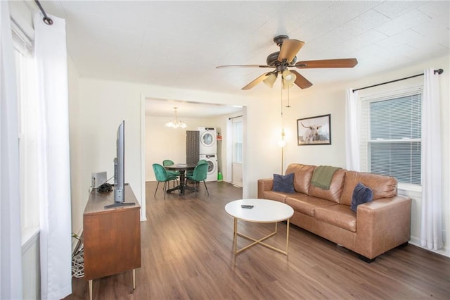 living room featuring stacked washer / drying machine, ceiling fan with notable chandelier, dark wood-type flooring, and a wealth of natural light