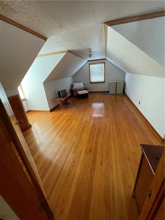 bonus room featuring lofted ceiling, a textured ceiling, and light wood-type flooring