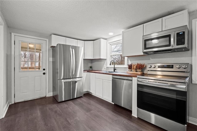 kitchen featuring appliances with stainless steel finishes, butcher block countertops, a sink, and white cabinets