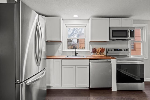 kitchen featuring butcher block countertops, dark wood-style flooring, stainless steel appliances, white cabinetry, and a sink