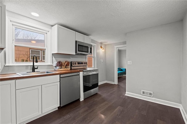 kitchen with stainless steel appliances, butcher block counters, visible vents, white cabinetry, and a sink