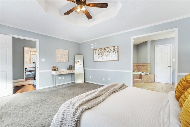 carpeted bedroom featuring a tray ceiling, ensuite bathroom, ceiling fan, and ornamental molding