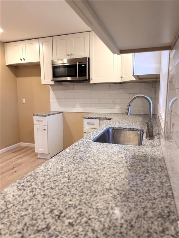 kitchen featuring backsplash, white cabinetry, sink, and light stone counters