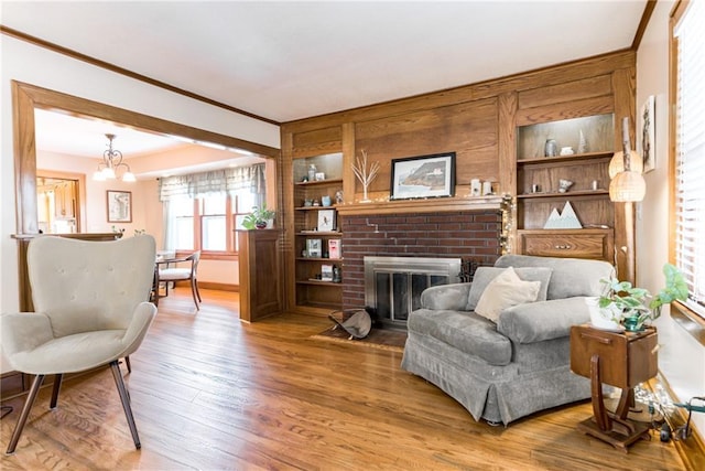 sitting room with a fireplace, a chandelier, hardwood / wood-style flooring, crown molding, and built in shelves