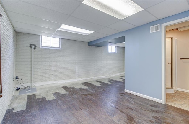 basement featuring hardwood / wood-style floors, a paneled ceiling, and brick wall