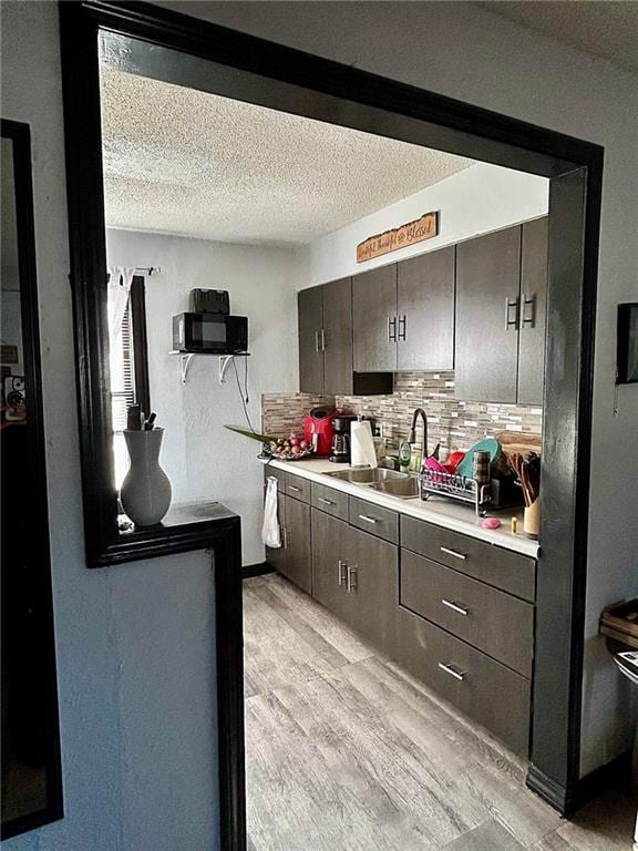 kitchen with a textured ceiling, tasteful backsplash, light hardwood / wood-style floors, and sink