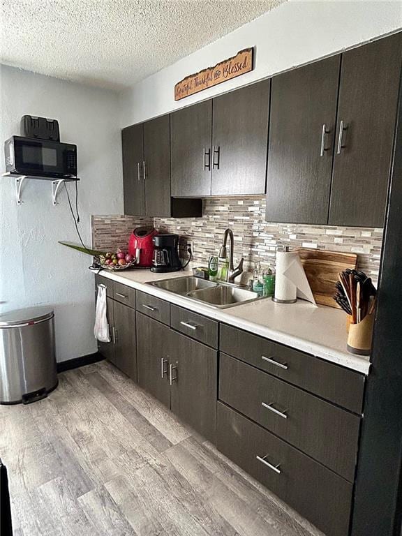 kitchen with light wood-type flooring, backsplash, a textured ceiling, dark brown cabinetry, and sink