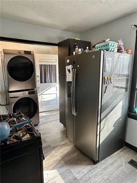 kitchen with a textured ceiling, stacked washer / drying machine, stainless steel fridge with ice dispenser, and black gas range