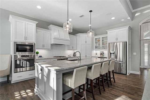 kitchen with stainless steel appliances, a kitchen island with sink, white cabinetry, and sink