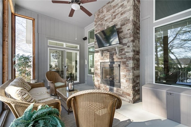 sunroom / solarium featuring ceiling fan, a wealth of natural light, and a stone fireplace