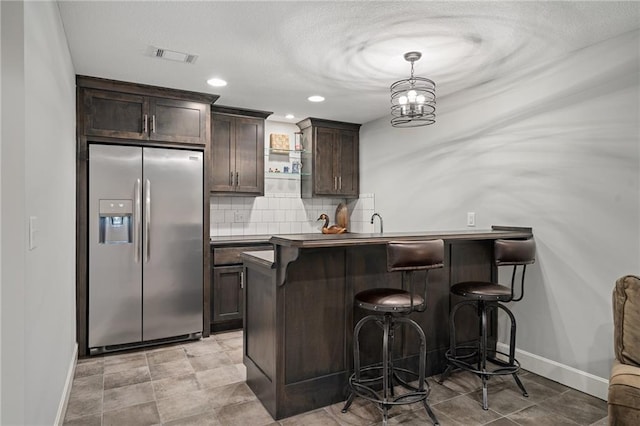 kitchen featuring hanging light fixtures, stainless steel fridge, kitchen peninsula, dark brown cabinets, and a breakfast bar area