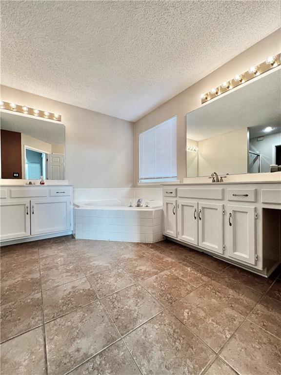 bathroom with tiled tub, vanity, and a textured ceiling