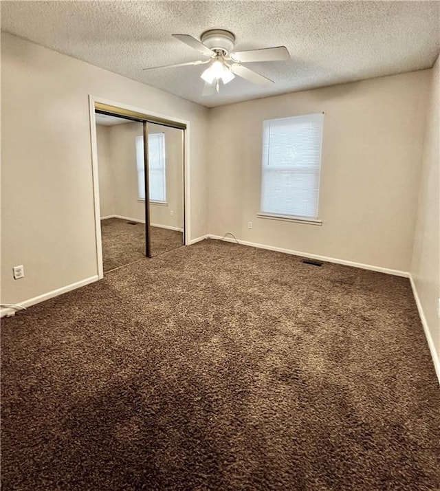 unfurnished bedroom featuring dark carpet, a textured ceiling, a closet, and ceiling fan