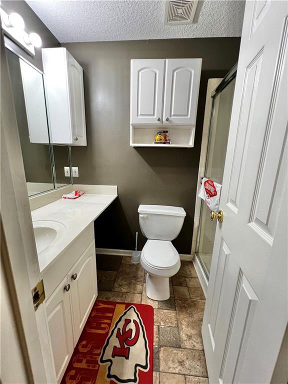 bathroom with vanity, toilet, a textured ceiling, and walk in shower