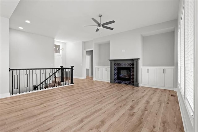 unfurnished living room with ceiling fan, a fireplace, and light wood-type flooring