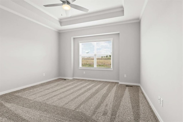 empty room with a raised ceiling, ornamental molding, carpet flooring, and ceiling fan