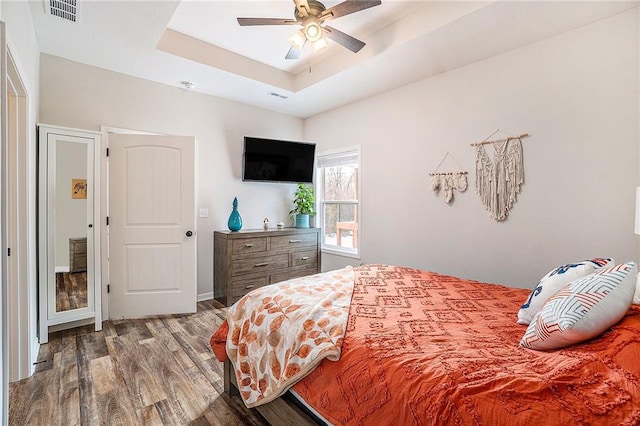 bedroom featuring ceiling fan, wood-type flooring, and a raised ceiling