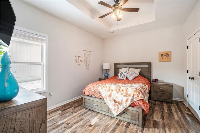 bedroom featuring ceiling fan, a tray ceiling, and dark hardwood / wood-style flooring