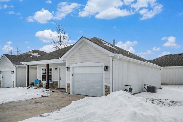 1740 S Park Dr, Tonganoxie, KS 66086 - snow covered property featuring a porch, a garage, stone siding, and central AC unit