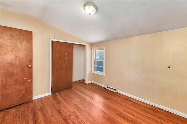 unfurnished bedroom featuring vaulted ceiling, light wood-type flooring, and a closet