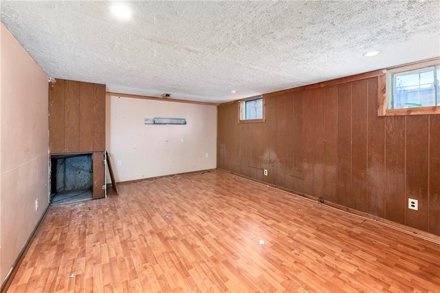 basement with wooden walls, light hardwood / wood-style flooring, and a textured ceiling