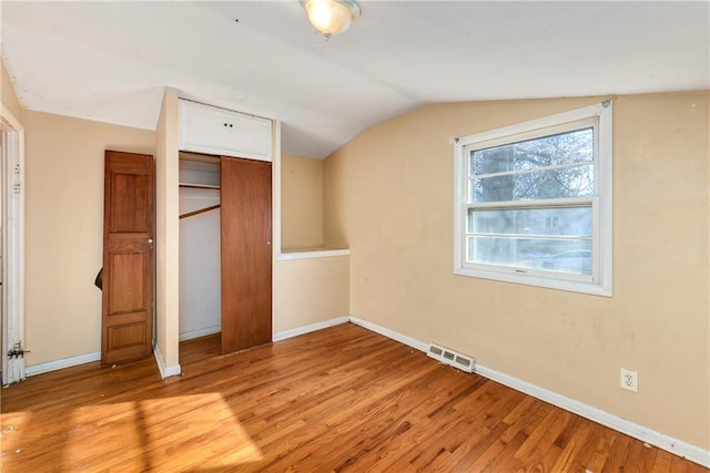 unfurnished bedroom with vaulted ceiling, a closet, and light wood-type flooring