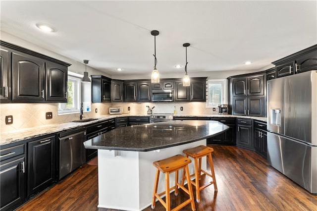 kitchen with sink, hanging light fixtures, dark stone countertops, a kitchen island, and stainless steel appliances