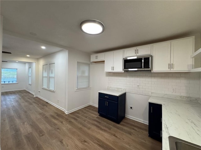 kitchen with blue cabinetry, white cabinetry, light stone counters, dark hardwood / wood-style floors, and decorative backsplash