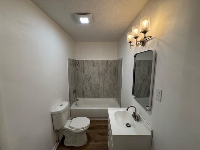 full bathroom with hardwood / wood-style floors, tiled shower / bath combo, vanity, toilet, and a textured ceiling