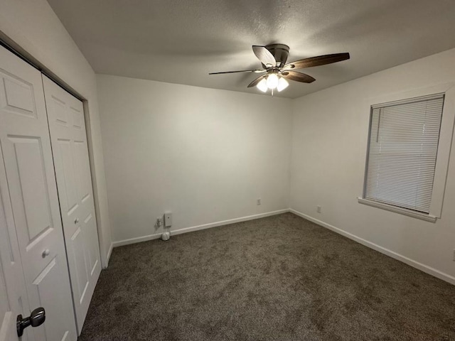 unfurnished bedroom with ceiling fan, a textured ceiling, a closet, and dark colored carpet