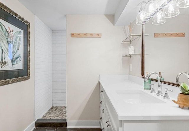 bathroom with tile patterned flooring, a tile shower, vanity, and baseboards