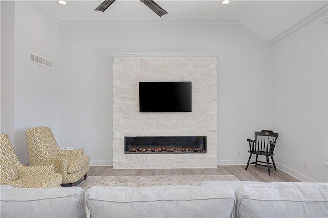 living room featuring lofted ceiling, crown molding, wood-type flooring, ceiling fan, and a fireplace