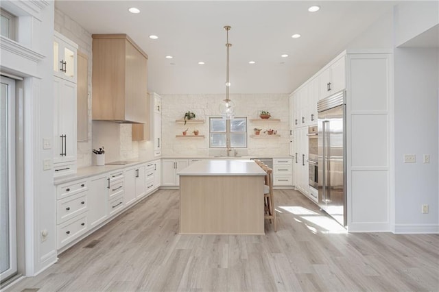 kitchen featuring hanging light fixtures, a center island, white cabinets, and light wood-type flooring