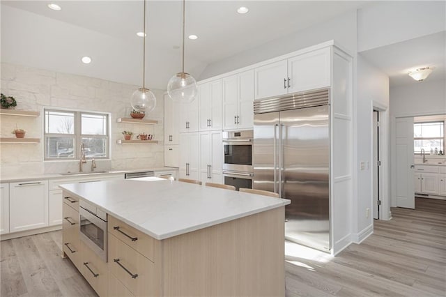 kitchen with sink, backsplash, a center island, built in appliances, and decorative light fixtures