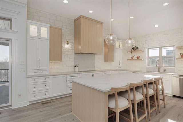 kitchen with sink, dishwasher, white cabinetry, a center island, and light hardwood / wood-style floors