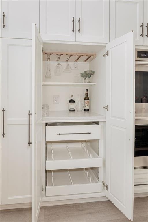 bar with white cabinetry, double oven, and light hardwood / wood-style floors