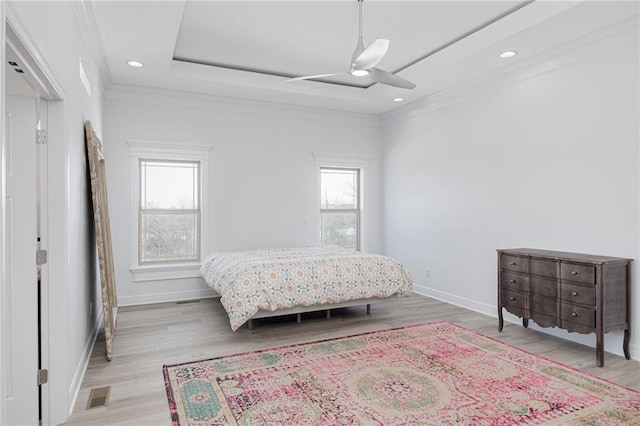 bedroom featuring multiple windows, light hardwood / wood-style flooring, a raised ceiling, and ceiling fan